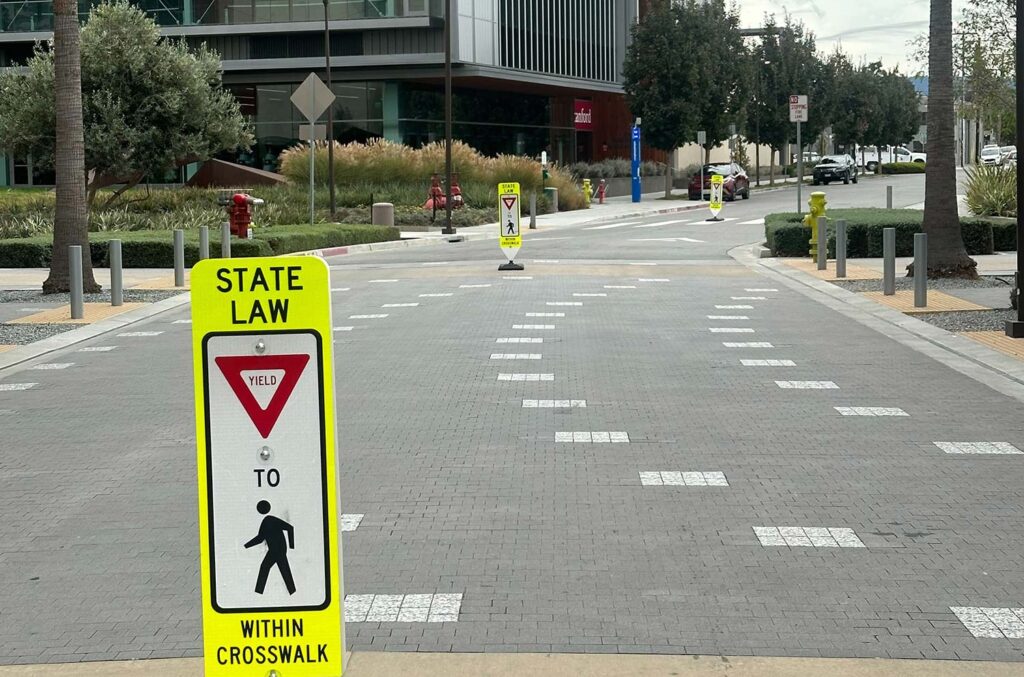 A crosswalk marker stands in the middle of a street on the Stanford Redwood Campus.