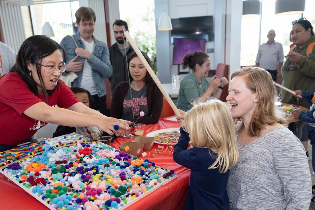 Mother and child helped by a Stanford community member participate in STEMfest, lifting pompom balls (Photo by Jim Gensheimer)